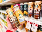 hand holding 2 starbucks coffee drinks in front of a target shelf