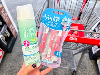 hand holding Gillette Venus disposable razors and Satin Care shave gel in front of CVS cart