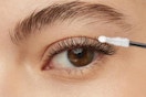 One brown eye with a well-groomed brow has a false lash and the glue topcoat combo is being applied to it.