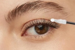 One brown eye with a well-groomed brow has a false lash and the glue topcoat combo is being applied to it.