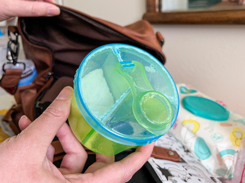 A person putting a munchkin baby formula dispenser into a diaper bag