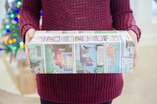 A person holding a box wrapped in newspaper.
