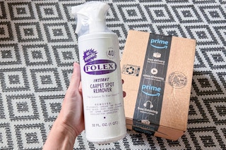 a hand holding a spray bottle in front of an Amazon box