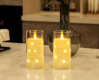 two flameless candles on a counter with a vase