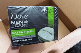 a hand holding a pack of bar soaps over a box