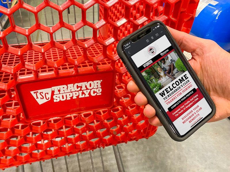 A person holding their phone displaying a welcome email from the TSC Neighbor's Club next to a Tractor Supply shopping cart.