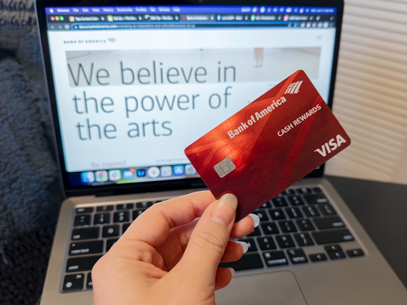 Someone holding their Bank of America card in front of a laptop displaying the information page about their Museums on Us program