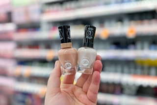 hand holding two bottles of nail polish in front of store shelves in beauty aisle