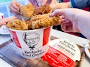 open bucket of kfc chicken on table with family hands pulling out multiple pieces of chicken