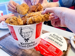 open bucket of kfc chicken on table with family hands pulling out multiple pieces of chicken