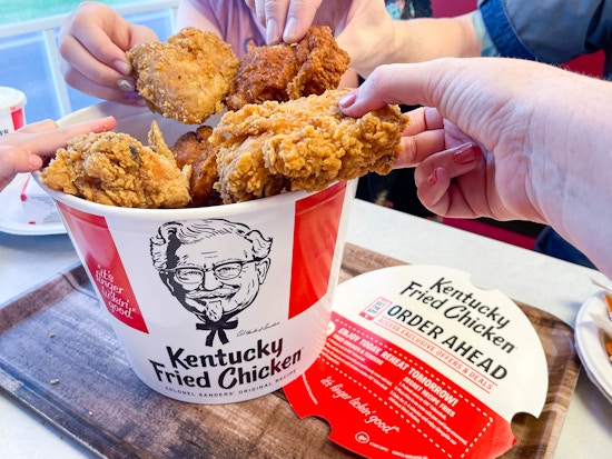 open bucket of kfc chicken on table with family hands pulling out multiple pieces of chicken