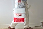 A 5-gallon paint bucket of Kilz Original Primer being carried into a room for DIY work