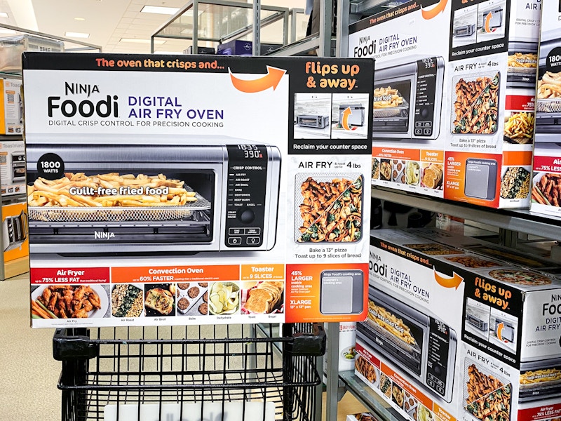 A Ninja Foodi air fryer sitting on top of a shopping cart next to a shelf of more air fryers at Belk.