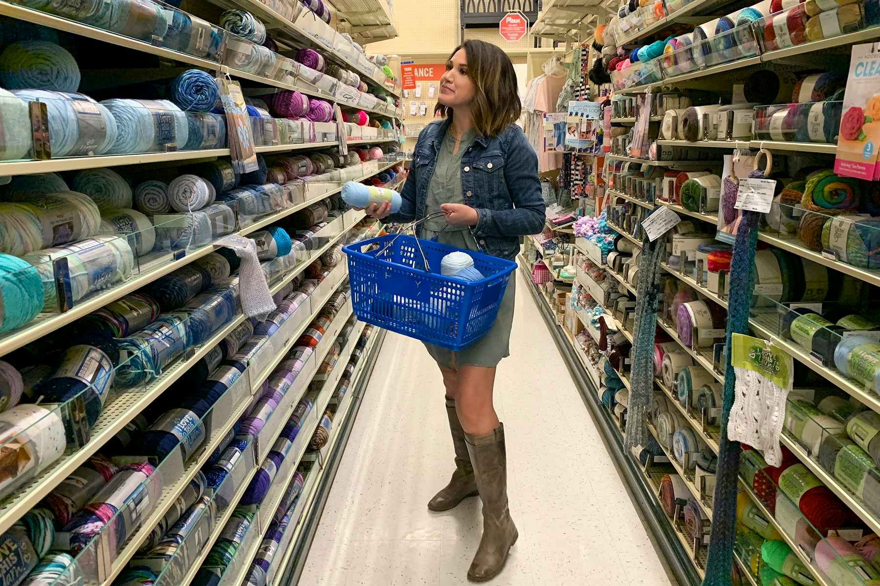 A woman filling a hand basket with yarn at Hobby Lobby.