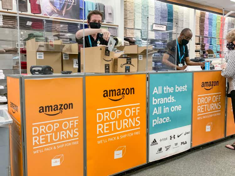 A Kohl's employee taping an Amazon return box at the Amazon Drop Off Returns counter inside Kohl's.
