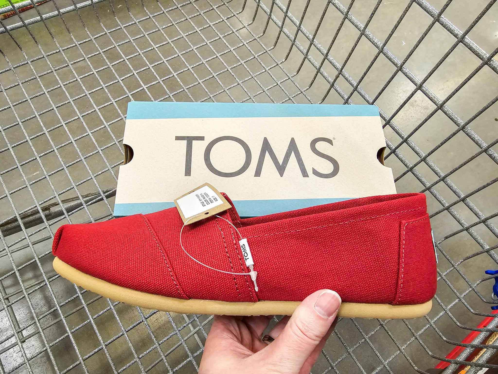 person holding a red toms shoe over a shoe box in a cart