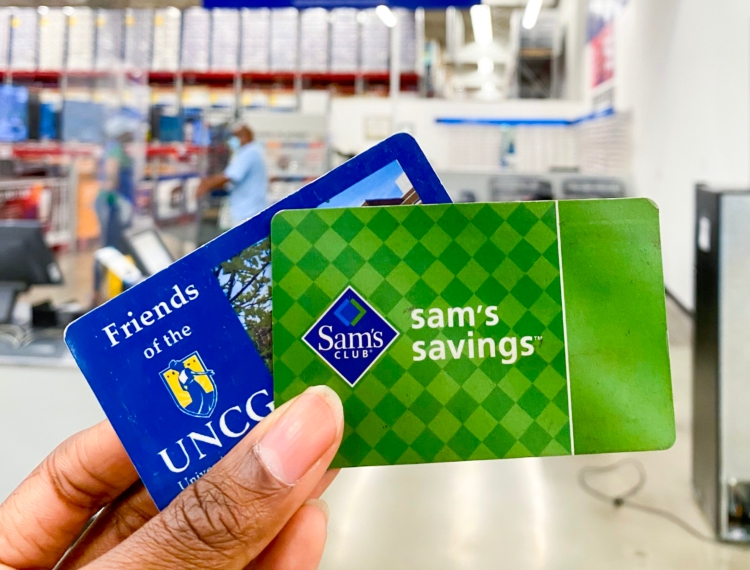 Hand holding Sam's savings card and Friends of UNCG card