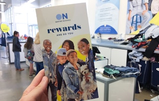 A person's hand holding up a brochure for Old Navy's reward program while standing in line for checkout at Old Navy.