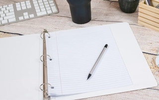 a white binder on a wooden surface with paper and a pen inside 