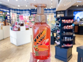 A hand soap held out by hand with the rest of the store in the background.