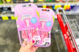 hand holding two packs of Venus Disposable razors next to a cvs shopping cart