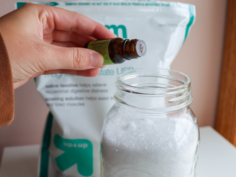 a person adding essential oils to a mason jar full of epsom salts