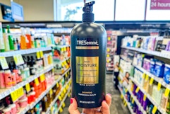 person holding a bottle of tresemme shampoo in an aisle