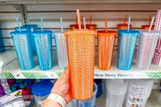 person holding an orange studded tumbler in front of blue and whit studded tumblers