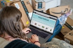 A woman shopping on Amazon on a laptop surrounded by Amazon boxes