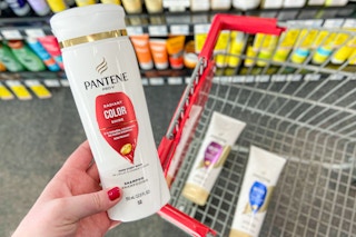 hand holding Pantene shampoo bottle in front of cart with other bottles inside