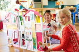 two girls playing with a barbie dollhouse