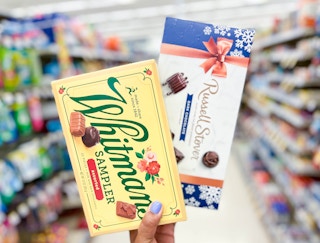 hand holding one box of Russell Stover and Whitman chocolates