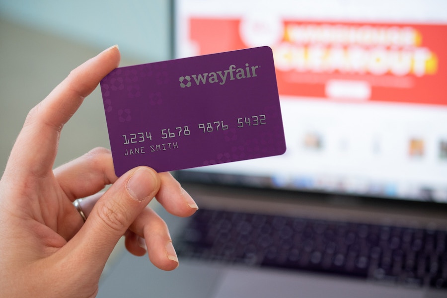 person holding wayfair credit card with homepage and laptop in background