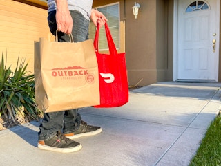 a DoorDash driver holding multiple delivery bags and walking up to the front door of a house