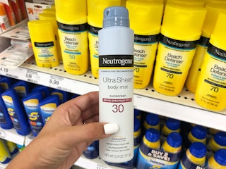 A person's hand holding a aerosol bottle of Neutrogena Ultra Sheer sunscreen in front of a shelf of sunscreen in Target.