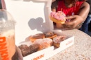Someone taking a heart shaped doughnut from a box on a table outside Dunkin