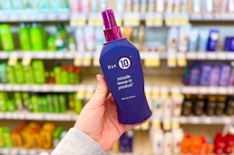 person holding a bottle of it's a 10 miracle leave-in product in front of shelves