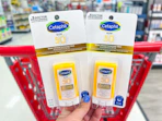 hand holding 2 cetaphil sunscreen sticks in front of a target cart