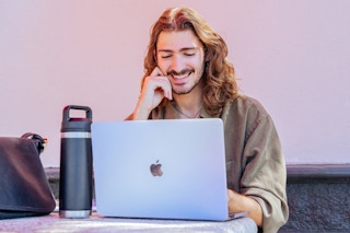 Person with long hair and a nose piercing looking at their laptop