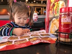 A child using a crayon to color on the kids menu at a booth in Red Robin.