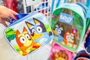 hand holding a bluey lunchbox in front of a bluey backpack at dollar tree