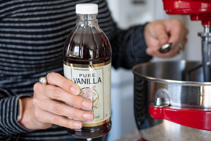 A person pouring a teaspoon full of pure vanilla into a mixing bowl