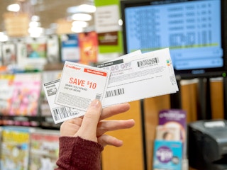 A person holding up printed coupons in front of a checkout register.