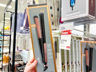 hand holding a conair infiniti pro flat iron in front of a shelf