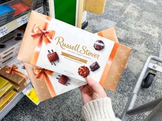 person holding 2 russell stover chocolate boxes