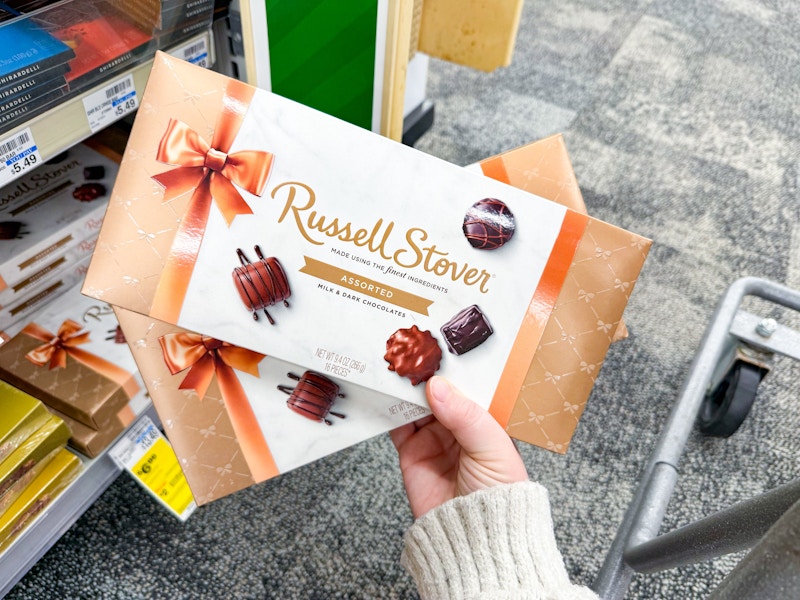 person holding 2 russell stover chocolate boxes