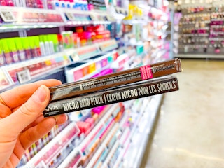 hand holding two nyx eyebrow pencils in walmart aisle