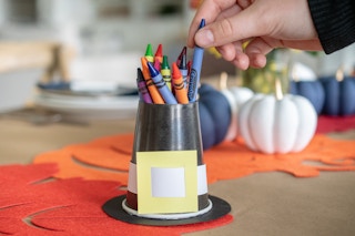 A person pulling a crayon out of a cup that looks like a pilgrims hat.