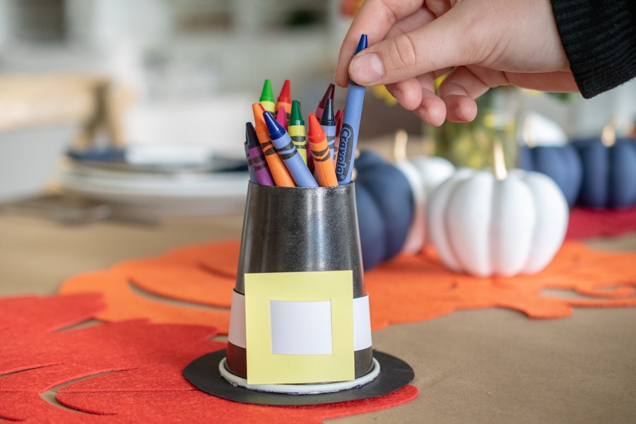 A person pulling a crayon out of a cup that looks like a pilgrims hat.