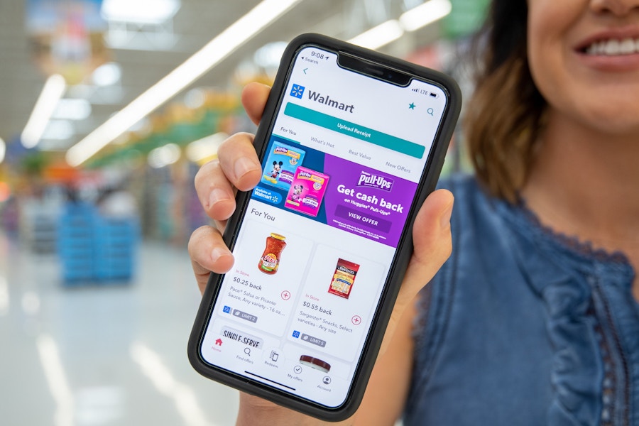 A woman holding a phone out in front of her with the ibotta app on the screen.